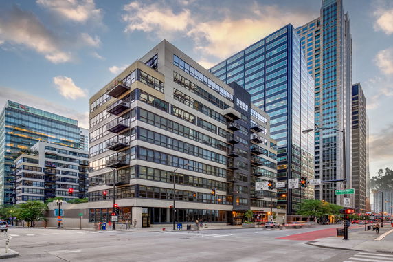 View of a modern multi-story building at a street corner, surrounded by other high-rise buildings.