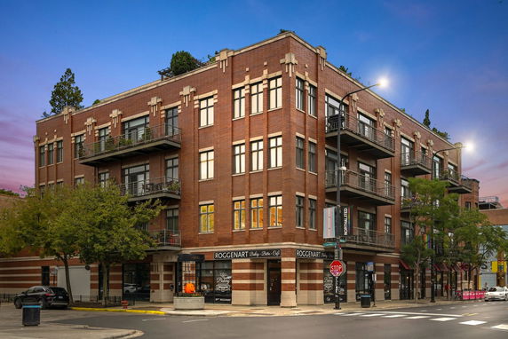 Front view of a multi-story brick building with balconies and shops on the ground floor.