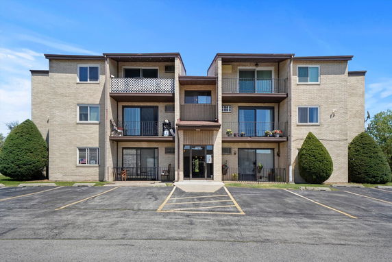 Front view of a three-story apartment building with balconies and a parking area.