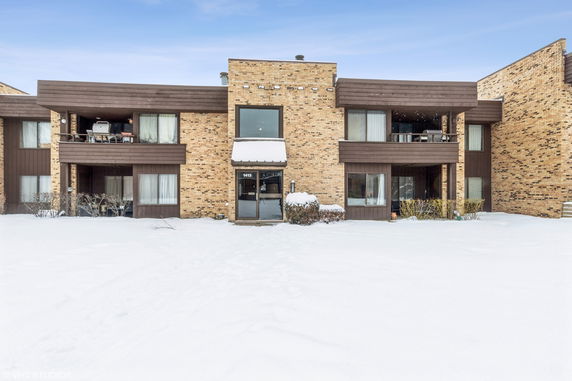 Front view of a multi-story brick building with balconies a snow-covered ground.