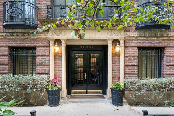 Front view of a brick building entrance with black double doors and decorative columns.