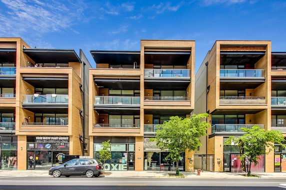 Front view of a modern multi-story building with glass balconies and brick facade.