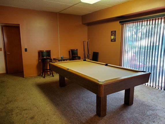 Room with a billiards table and chairs, featuring sliding glass doors.