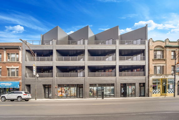 Front view of a modern multi-story building with large balconies and distinctive roof design.
