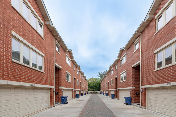 Front view of a series of multi-story brick houses with garages, lined along a central pathway.