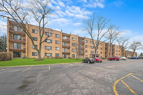 Front view of a multi-story apartment building with balconies and a parking area.