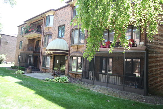 Front view of a multi-story brick apartment building with glass windows and covered entryway.