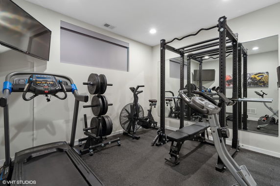 Interior view of a home gym with exercise equipment including a treadmill, weights, and a stationary bike.