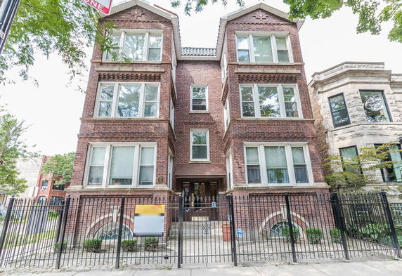 Front view of a multi-story brick building with large windows and a gated entrance.