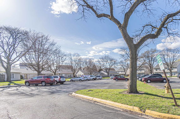 Outdoor parking area with several cars and residential buildings in the background.