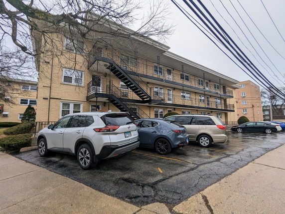 Front view of a three-story apartment building with an outdoor staircase and multiple cars parked in front.