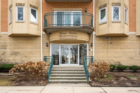 Front view of a condominium building entrance with stairs and balcony above.