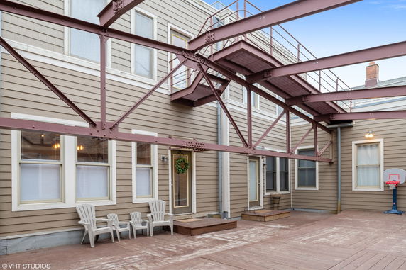 Outdoor area with external view of a building showing multiple windows and doors, metal structure overhead, and a small basketball hoop.