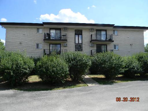 Front view of a multi-story building with balconies and shrubs in front.