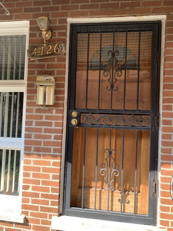 Front view of a brick house entrance with a decorative metal screen door.