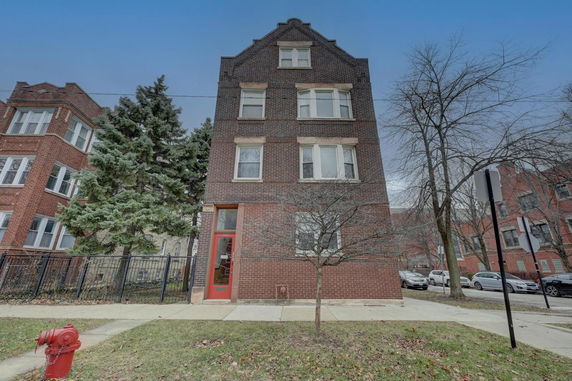 Front view of a multi-story brick building with a red entry door.