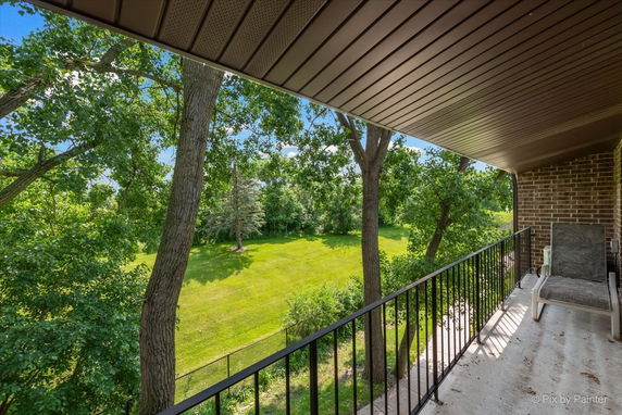 View of surrounding green area from a building balcony with trees and grass.