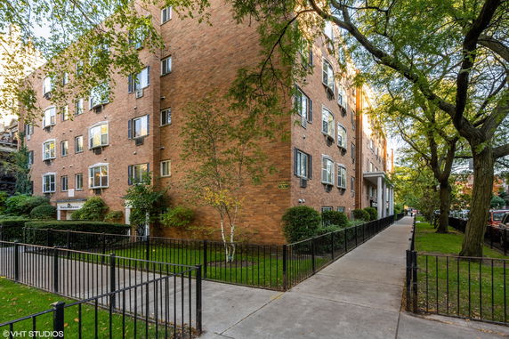 Front view of a multi-story brick apartment building with several windows and air conditioning units.