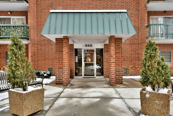Front view of a brick building entrance with a small awning and the number 555 above the glass door.