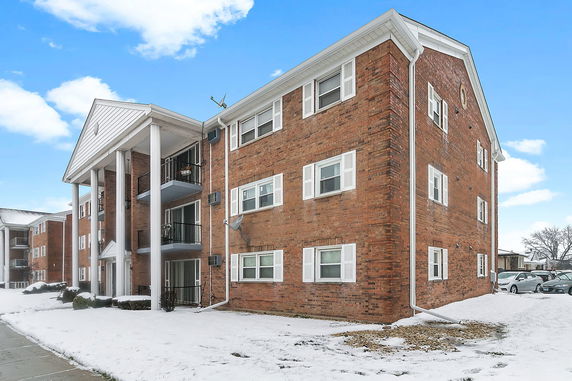 Front view of a multi-story brick apartment building with balconies and white columns.