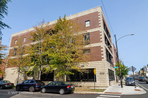 Front view of a four-story brick building with large windows and surrounding trees.
