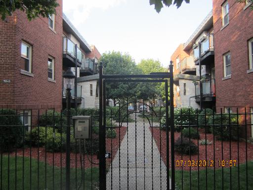 Front view of two multi-story brick buildings with balconies and a central gated entrance.