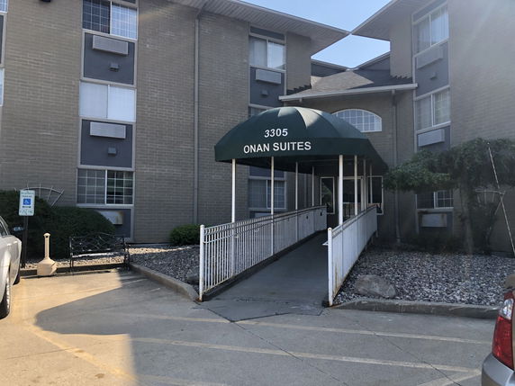 Front view of a multi-story building with a ramp entrance and awning labeled 'Onan Suites'.