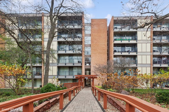 Front view of a multi-story apartment building with balconies and a landscaped walkway.