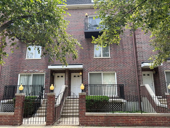 Front view of a multi-story brick townhouse with balconies and white doors.