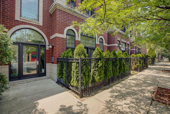 Front view of a multi-story brick building with large windows and a gated garden area.