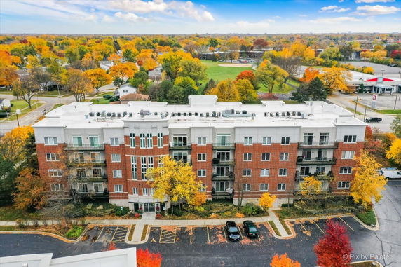 View of a multi-story brick and white building with a flat roof surrounded by fall foliage.