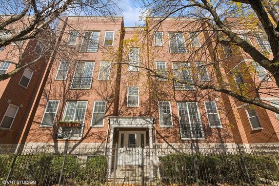 Front view of a brick multi-story apartment building with multiple windows and a gated entrance.