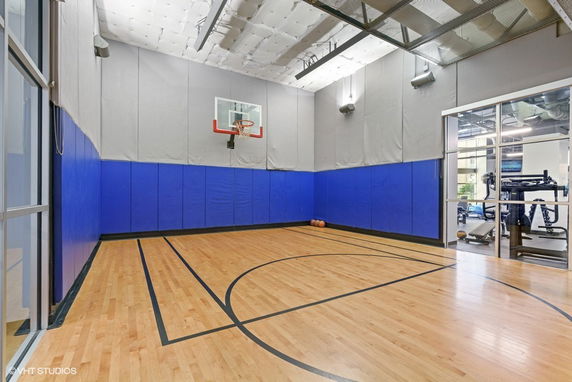 Indoor basketball court with a wooden floor and blue padded walls.
