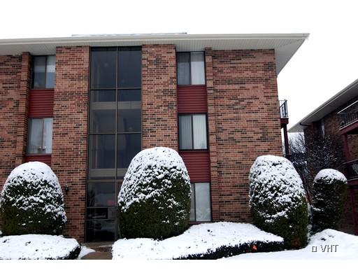 Front view of a brick apartment building in winter with snow-covered shrubs.