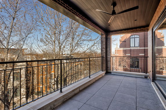 Balcony overlooking nearby buildings with tiled floor and ceiling fan.