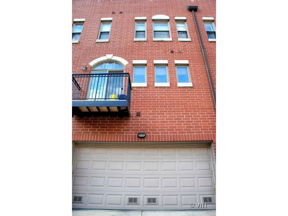 Front view of a multi-story brick building with a balcony and garage door.
