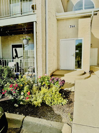 Front view of a building entrance with a small patio and flowering plants.