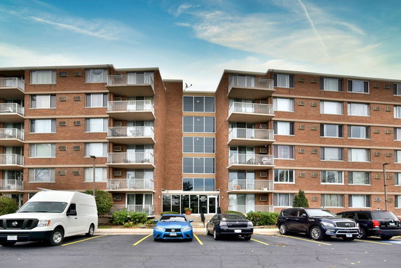 Front view of a multi-story residential apartment building with a parking area in front.