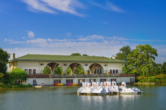 Front view of a building with arched openings, situated by a lake with swan-shaped pedal boats.