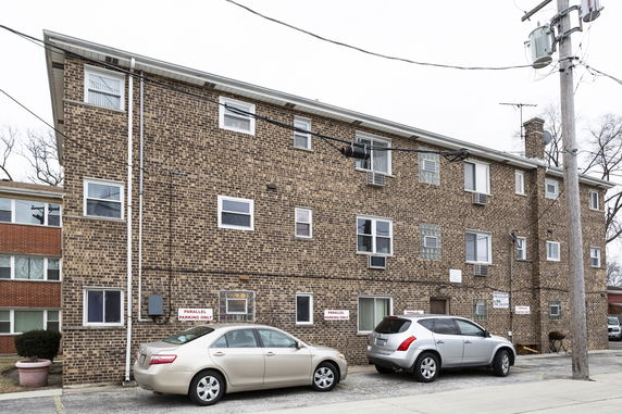 Front view of a multi-story brick building with several windows and parked cars.