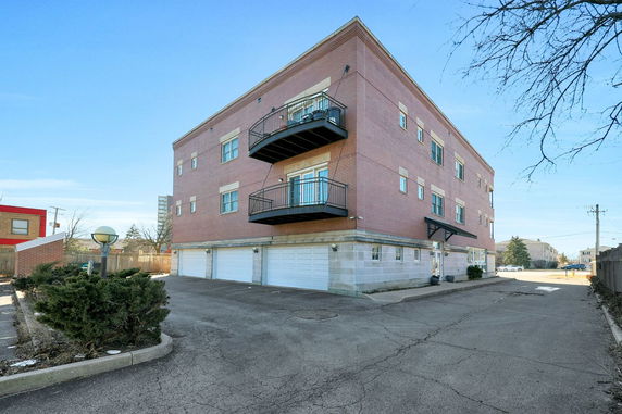 Front view of a multi-story brick building with balconies and a row of garage doors at the base.