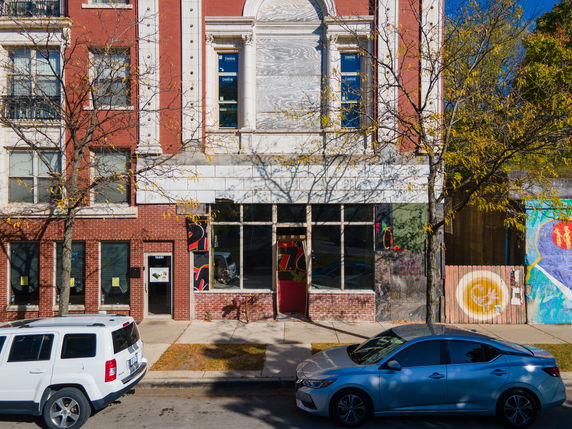 Front view of a multi-story building with brick facade and boarded windows.