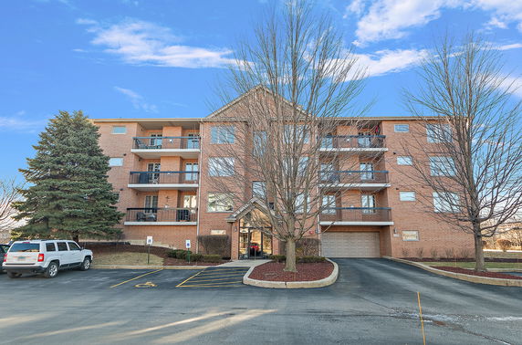 Front view of a multi-story brick apartment building with balconies and a parking area.