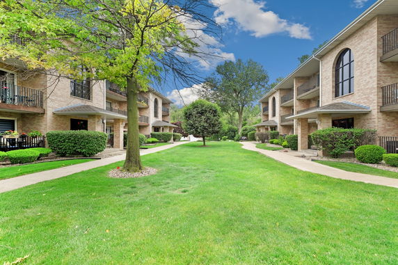 Front view of a brick apartment building with balconies and a landscaped lawn.
