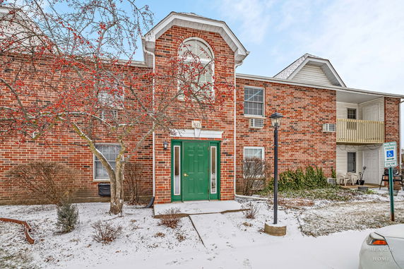 Front view of a brick two-story building with a green entrance door and an arched window above.