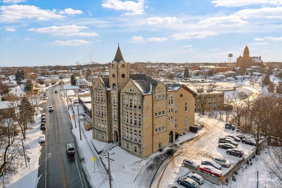 Front view of a large stone building with multiple peaked roofs and a central tower in a snowy urban area.