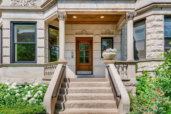 Front view of a house with decorative columns and steps leading to a wooden door.