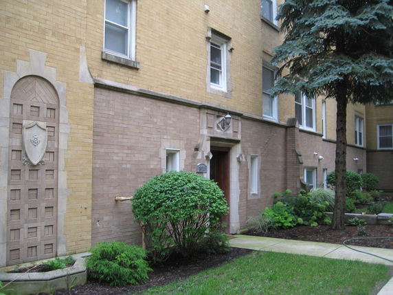 Front view of a multi-story brick building with decorative stone elements and a small garden area.
