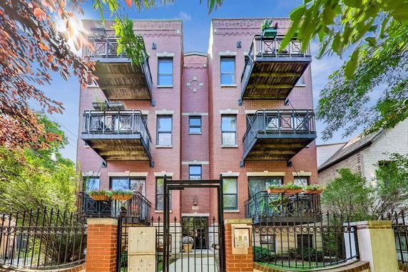 Front view of a multi-story brick building with balconies and a gated entrance.