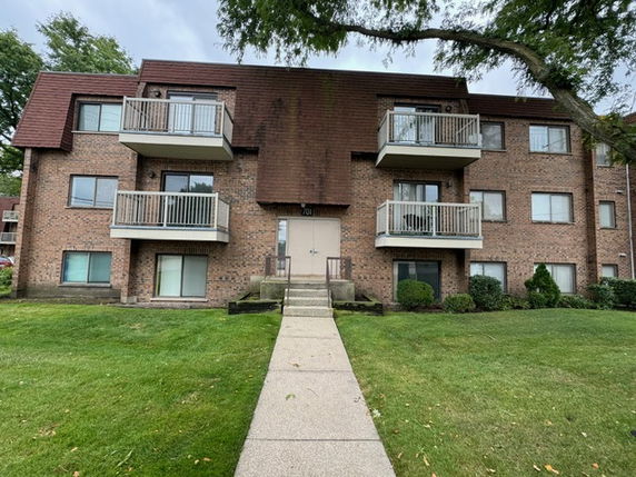 Front view of a three-story brick apartment building with balconies.